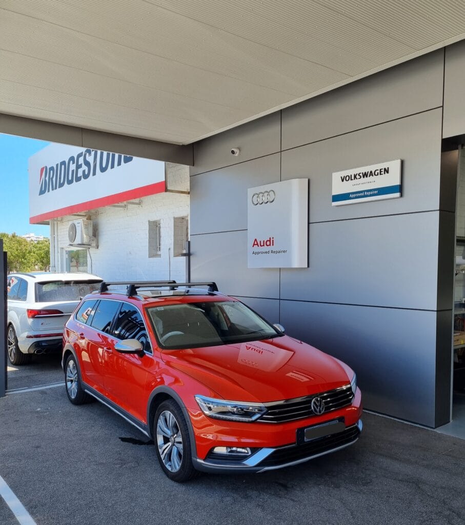 Red volkswagen car outside an Audi Approved Repairer workshop entrance.