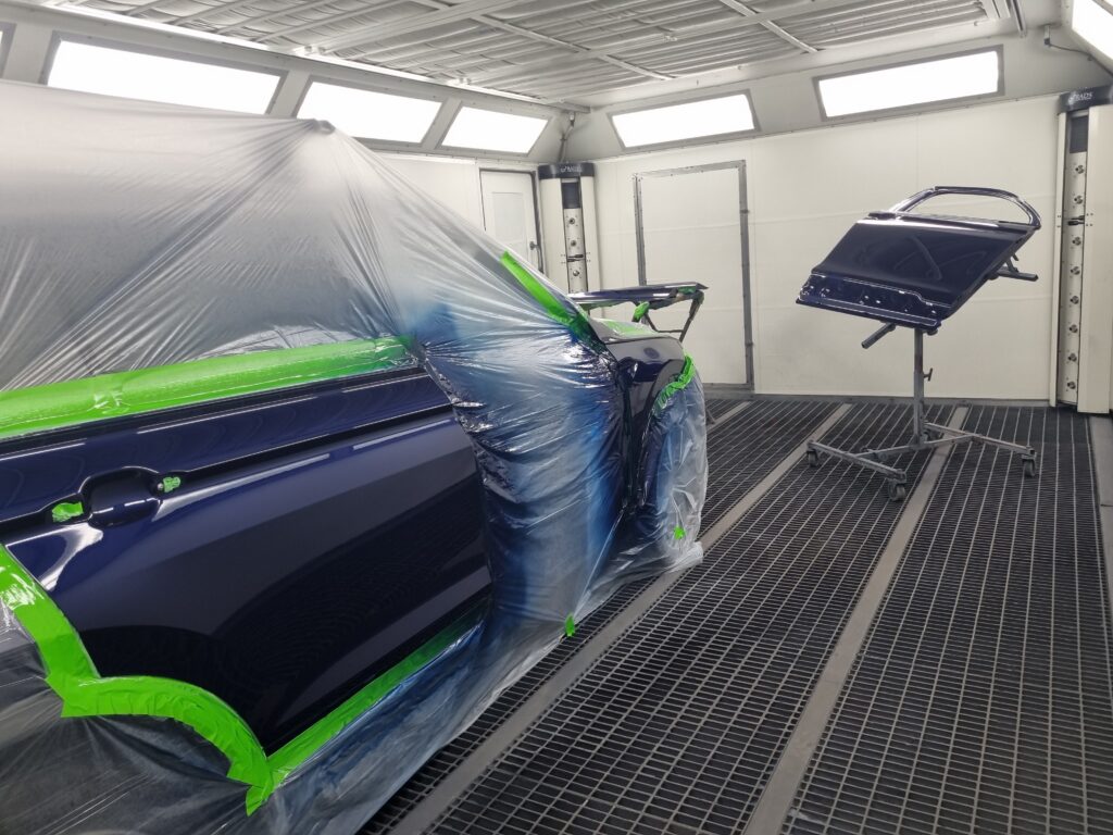 Vehicle body panel and door prepared for repainting inside a spray booth with protective masking and fresh paint finish.